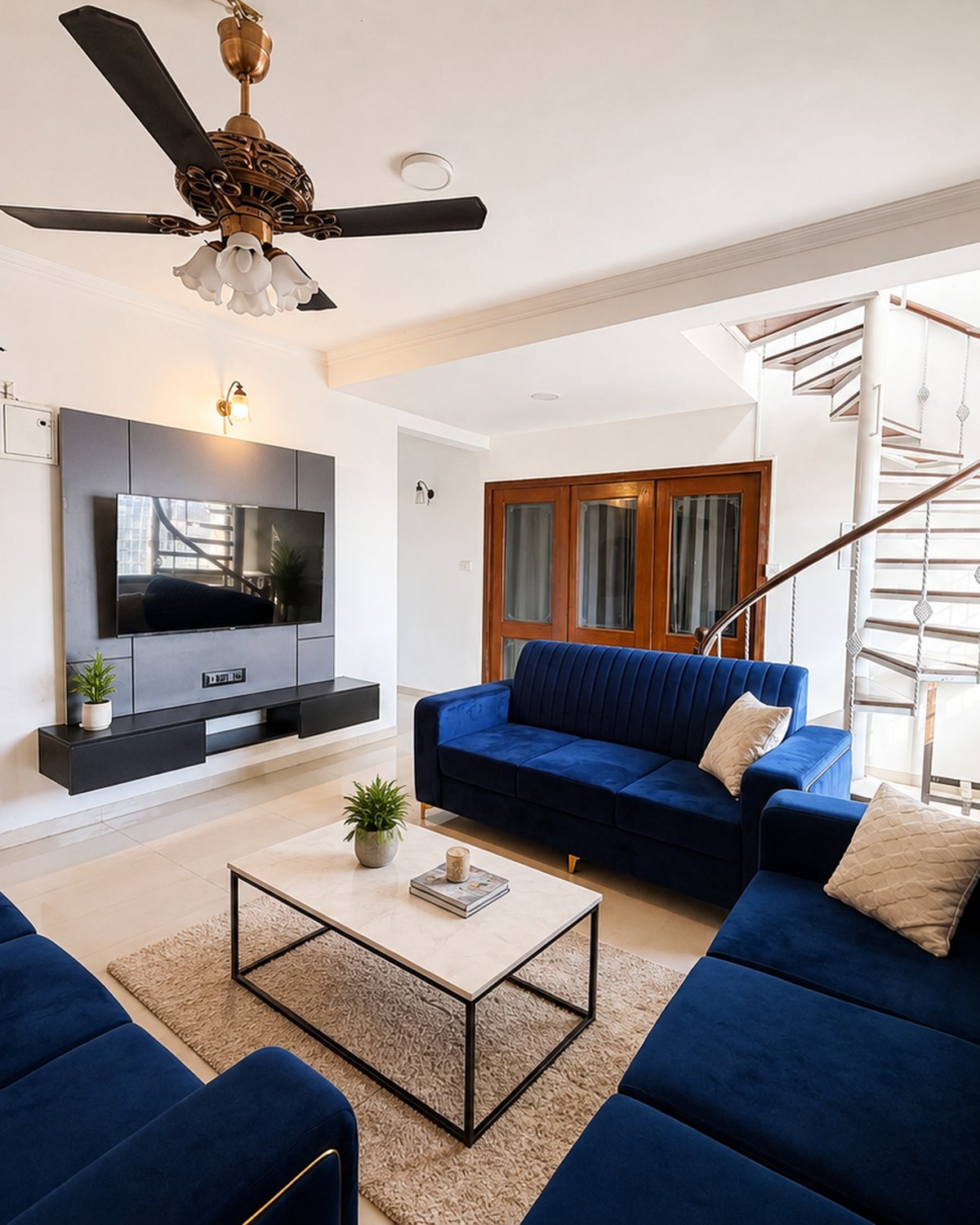 Sunlit shared living room with blue velvet sofas, TV wall and spiral staircase at Go GenZ Stays