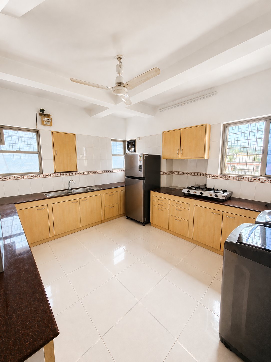 Spacious shared kitchen with wooden cabinets, gas stove and fridge — Go GenZ Stays girls PG
